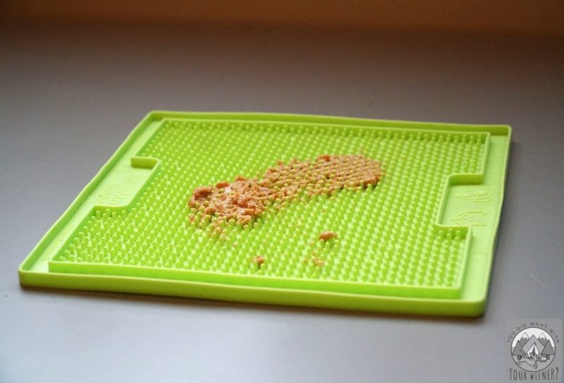 Green plastic lick mat with ridges with peanut butter smeared onto it.